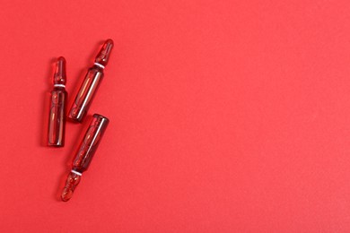 Photo of Glass ampoules with liquid on red background, top view. Space for text