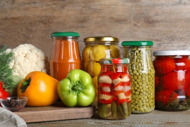 Photo of Glass jars with pickled vegetables on wooden table against brown background