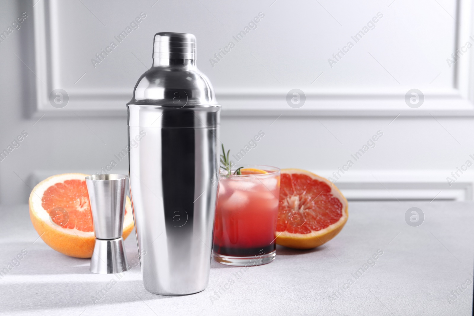 Photo of Metal shaker, delicious cocktail, jigger and grapefruit on light grey table