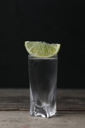 Shot of vodka with lime slice on wooden table