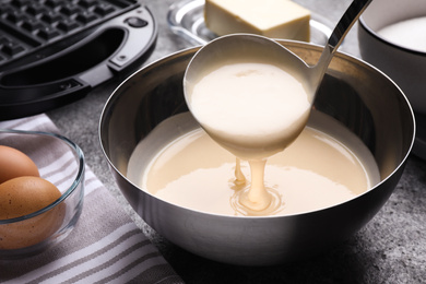 Ladle with dough for Belgian waffles over bowl, closeup