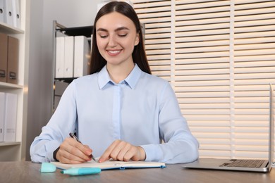 Happy woman taking notes at wooden table in office, space for text