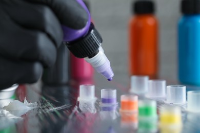 Photo of Tattoo artist dripping purple tattoo ink into cap on table, closeup