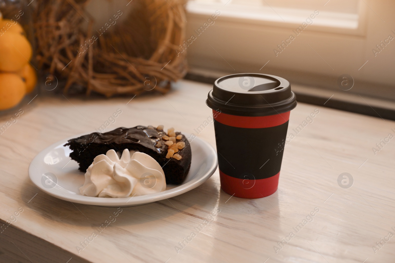 Photo of Tasty coffee in takeaway paper cup and dessert on wooden table indoors