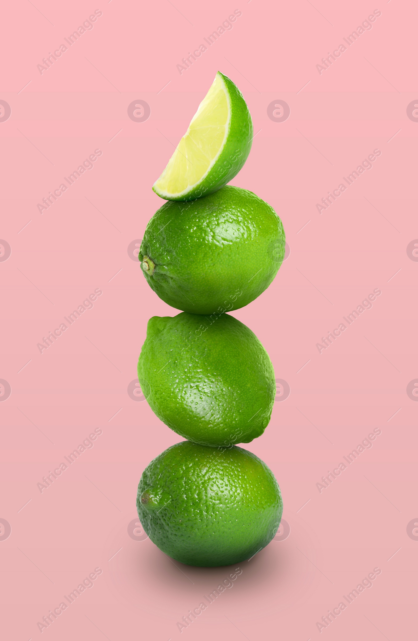 Image of Stacked whole and cut limes on pink background