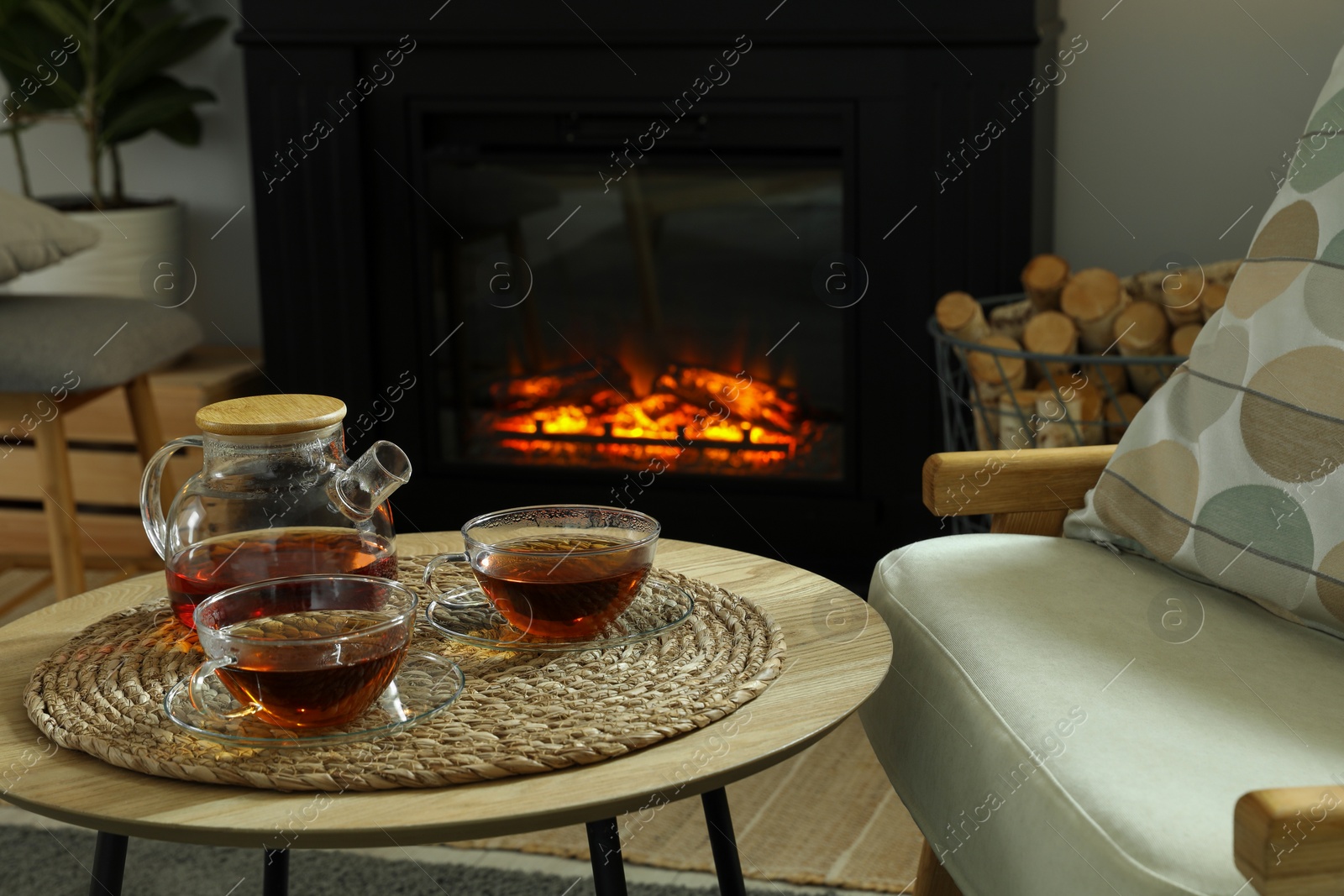 Photo of Teapot and cups of drink on coffee table near stylish fireplace in cosy living room. Interior design