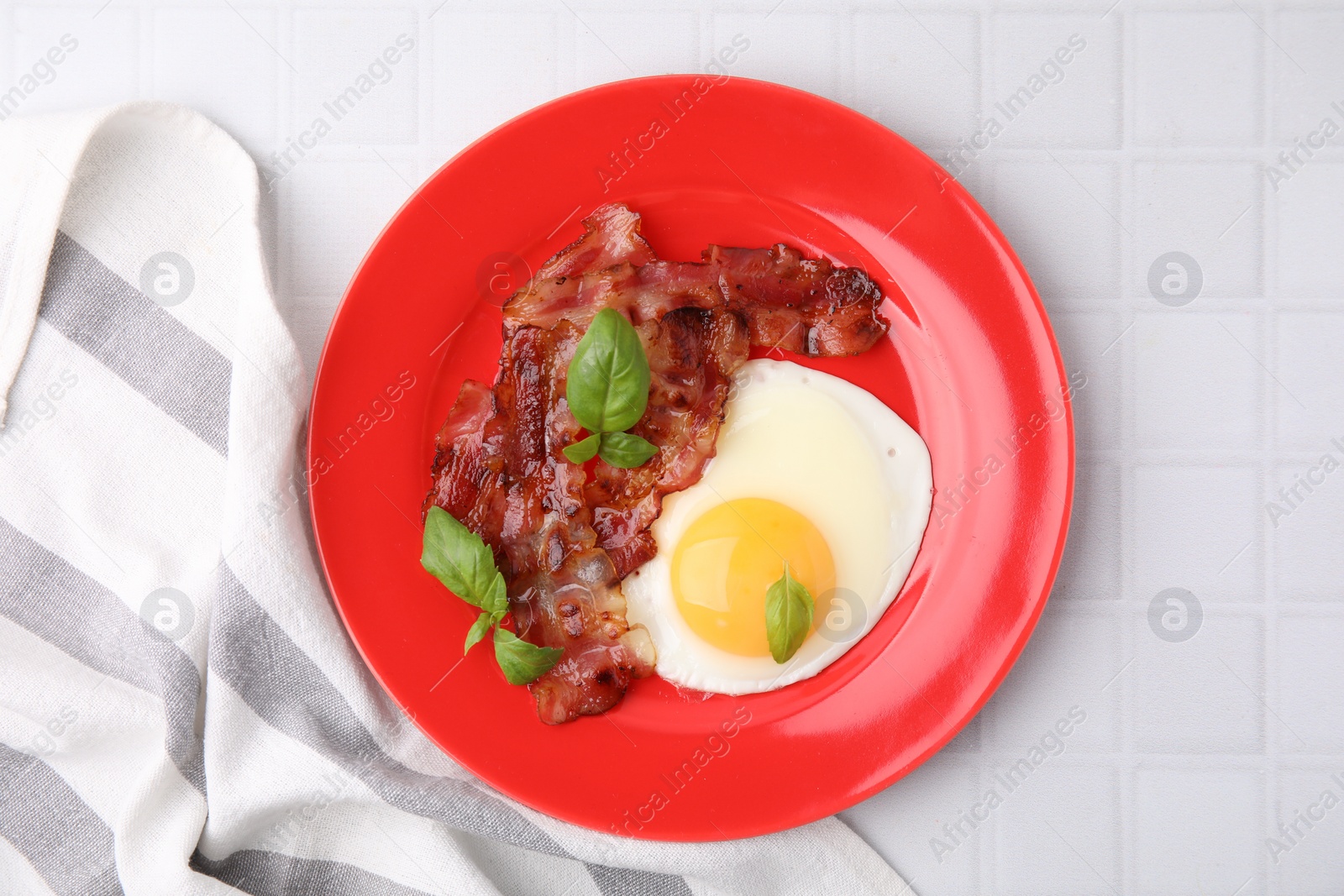 Photo of Fried egg, bacon and basil on white tiled table, top view