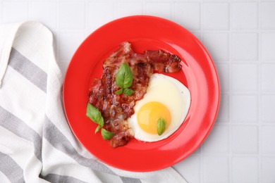 Fried egg, bacon and basil on white tiled table, top view