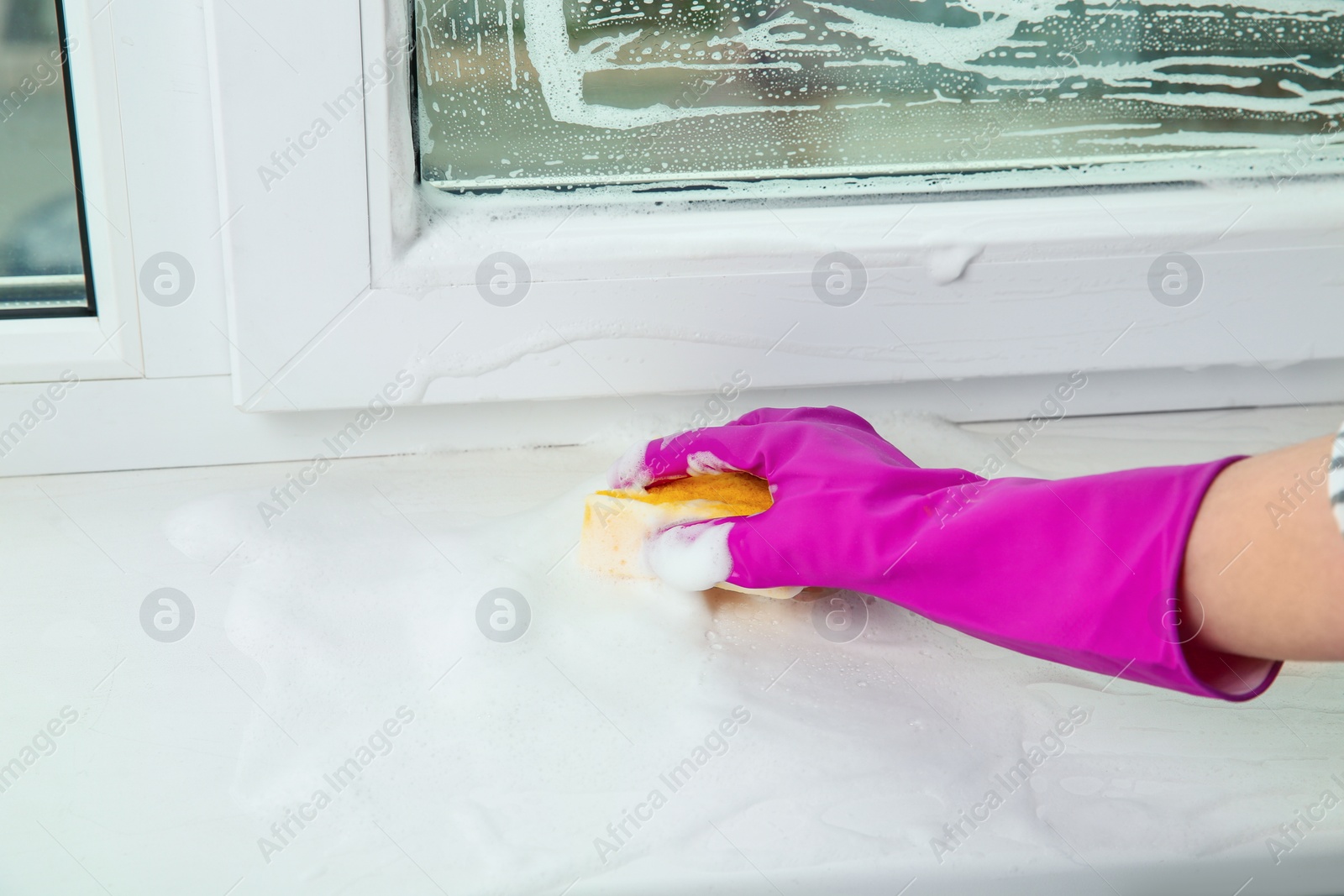 Photo of Woman cleaning window sill with sponge indoors, closeup