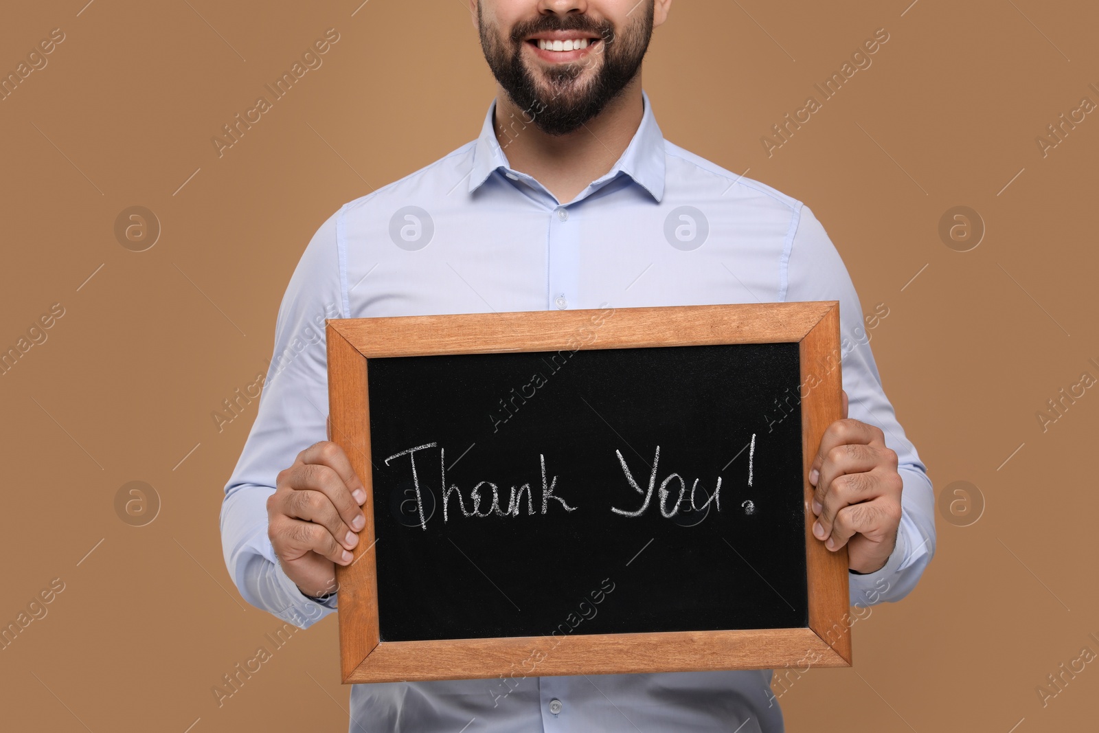 Photo of Man holding small chalkboard with phrase Thank You on brown background, closeup