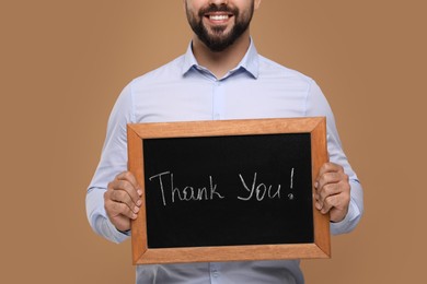 Photo of Man holding small chalkboard with phrase Thank You on brown background, closeup