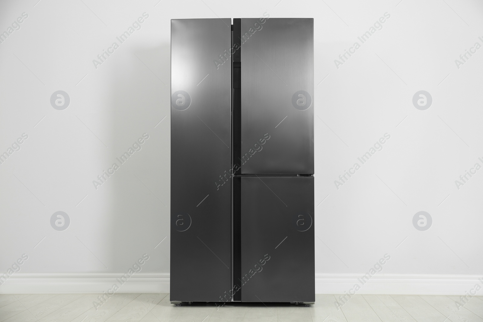 Photo of Modern refrigerator near light grey wall. Home appliance