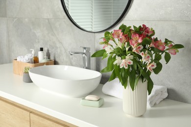 Photo of Vase with beautiful Alstroemeria flowers and toiletries near sink in bathroom