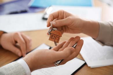 Photo of Real estate agent giving key with trinket to client in office, closeup