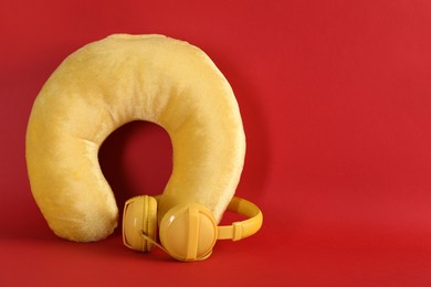 Photo of Yellow travel pillow and headphones on red background, space for text