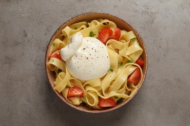 Photo of Bowl of delicious pasta with burrata and tomatoes on grey table, top view