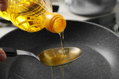 Photo of Woman pouring cooking oil from bottle into spoon, closeup