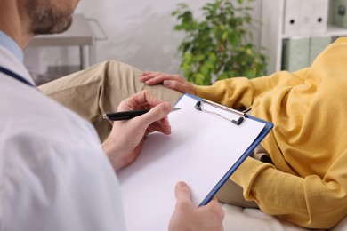 Doctor writing down patient's complaints during consultation in clinic, closeup