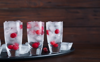 Photo of Shot glasses with vodka, ice and cranberries on table against wooden background