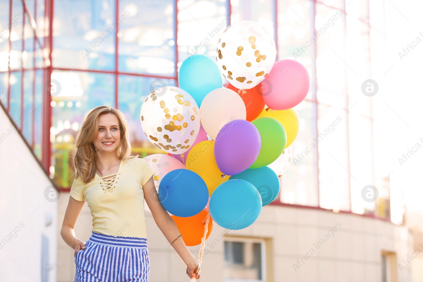 Photo of Young woman with colorful balloons outdoors on sunny day