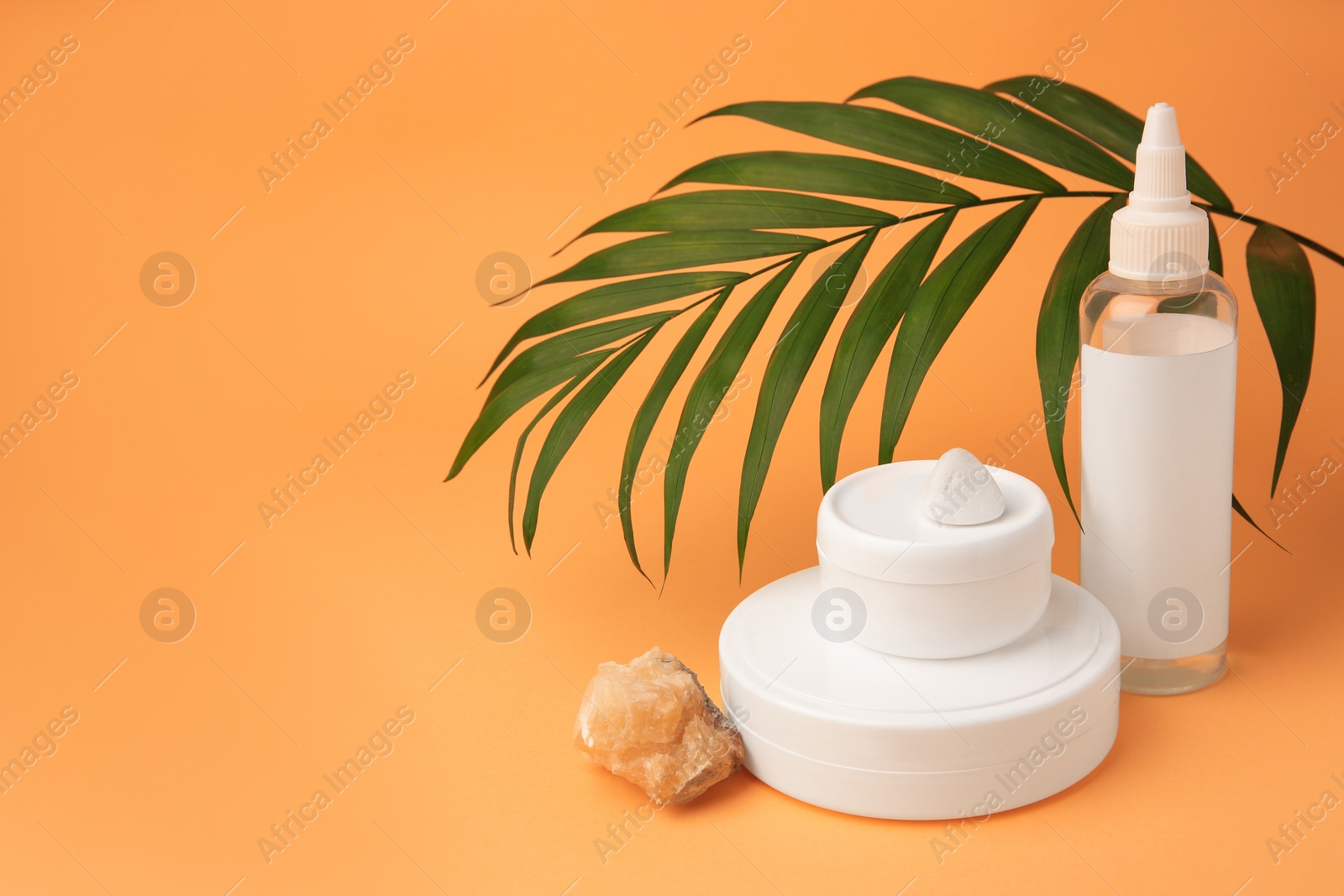 Photo of Cosmetic products, quartz gemstone and palm leaf on orange background, space for text