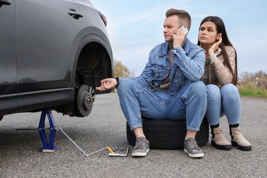 Young man calling to car service on roadside. Tire puncture