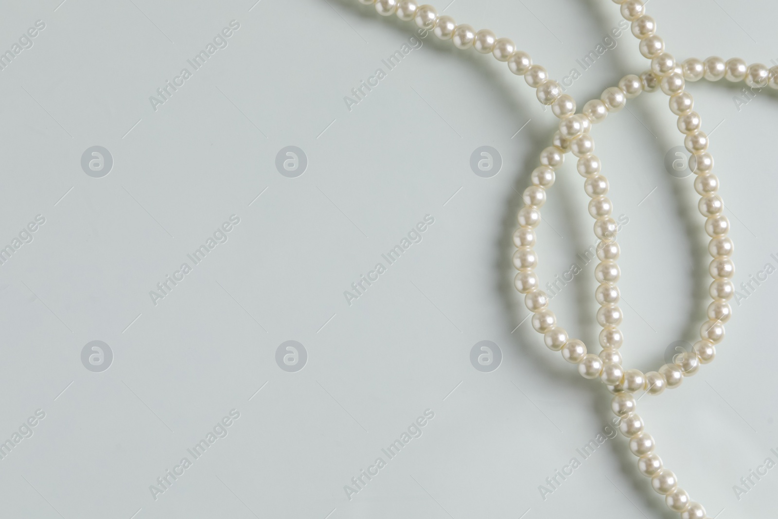Photo of Elegant pearl necklace on white table, top view. Space for text