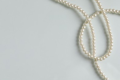 Elegant pearl necklace on white table, top view. Space for text