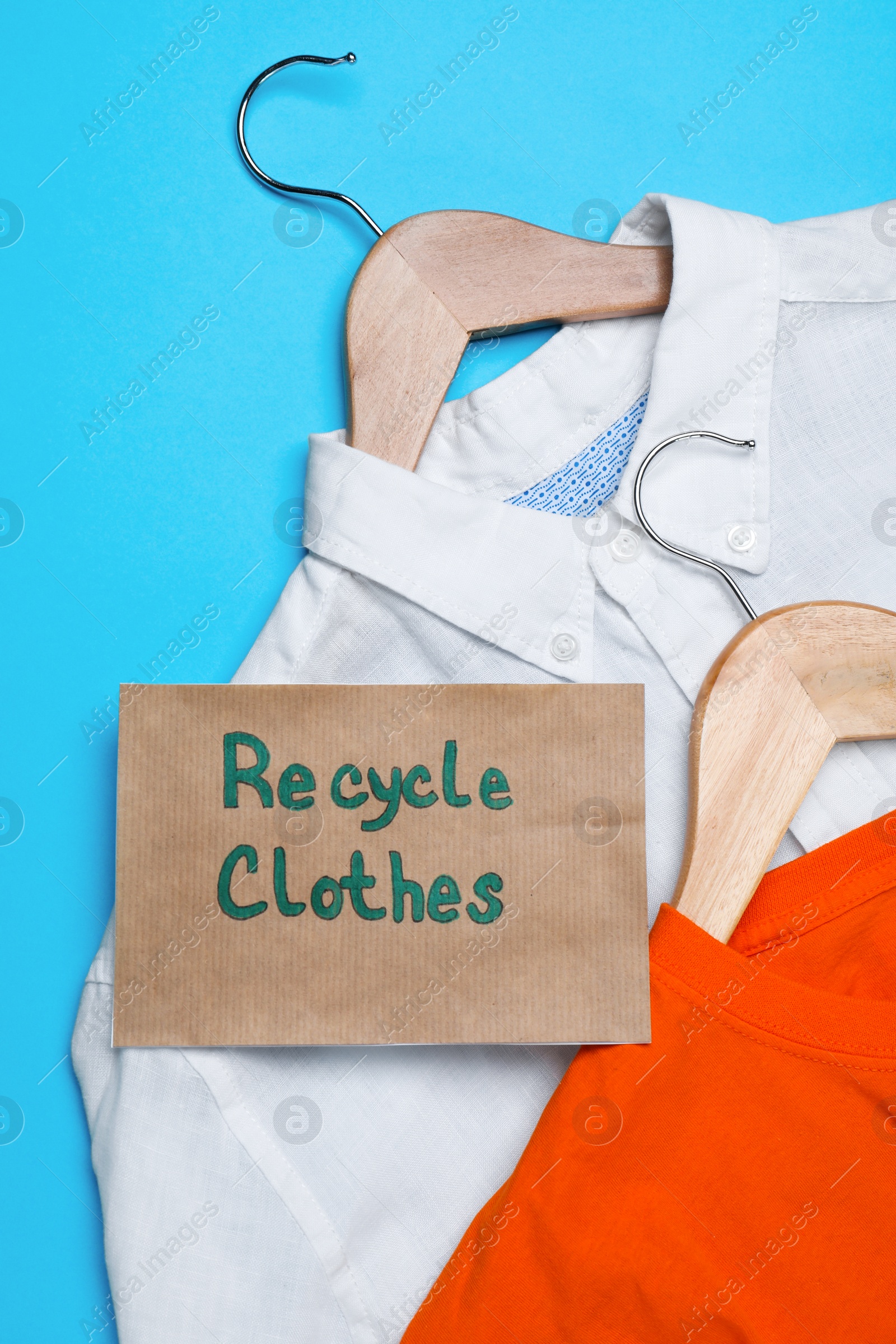 Photo of Different clothes with recycling label and hangers on light blue background, flat lay