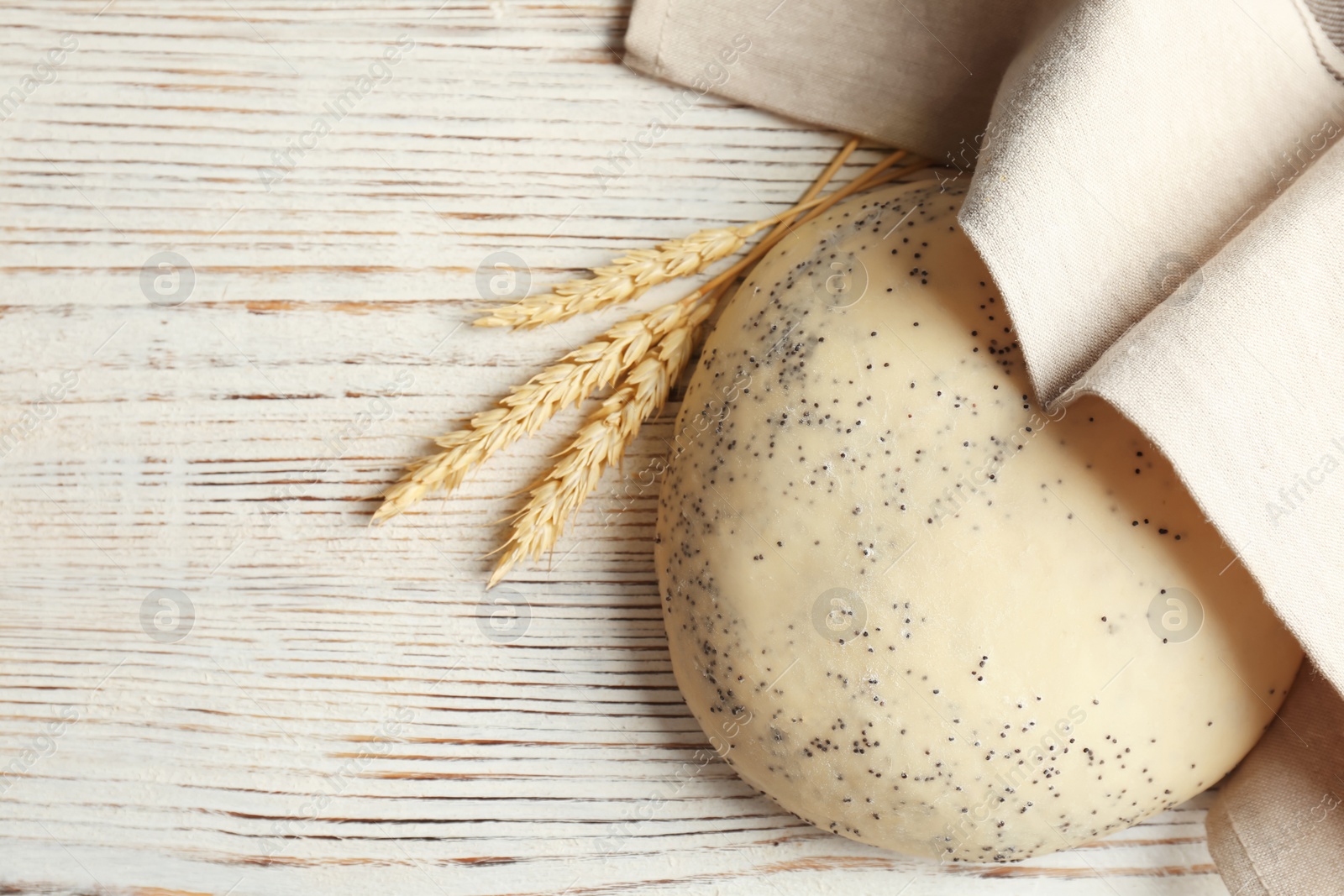 Photo of Raw dough with poppy seeds under towel on wooden table