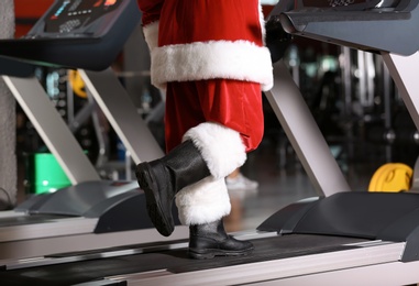 Authentic Santa Claus training on treadmill in modern gym, focus on legs