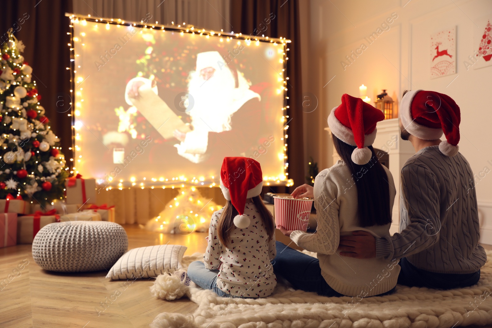 Photo of Family watching movie on projection screen in room decorated for Christmas, back view. Home TV equipment