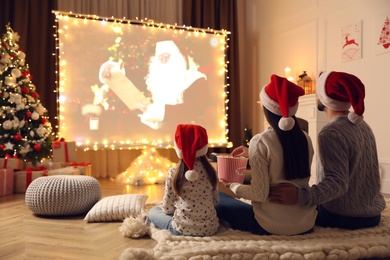 Photo of Family watching movie on projection screen in room decorated for Christmas, back view. Home TV equipment