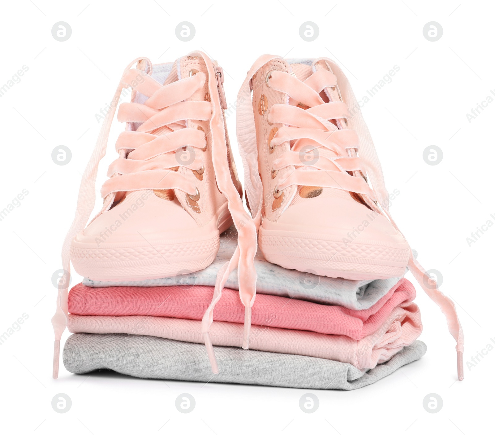 Photo of Stylish child shoes and stack of clothes on white background