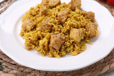 Photo of Plate of delicious rice with chicken on wicker mat, closeup