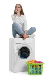 Upset woman on washing machine with laundry against white background