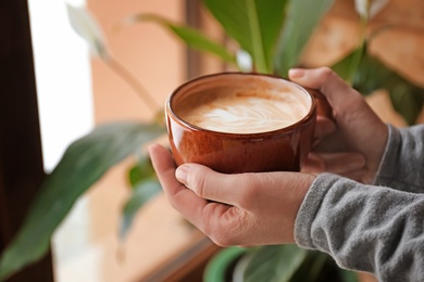 Photo of Woman holding cup of aromatic coffee with foam, closeup