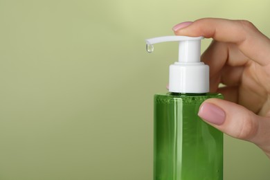 Photo of Woman using cleansing gel on pale olive background, closeup. Space for text