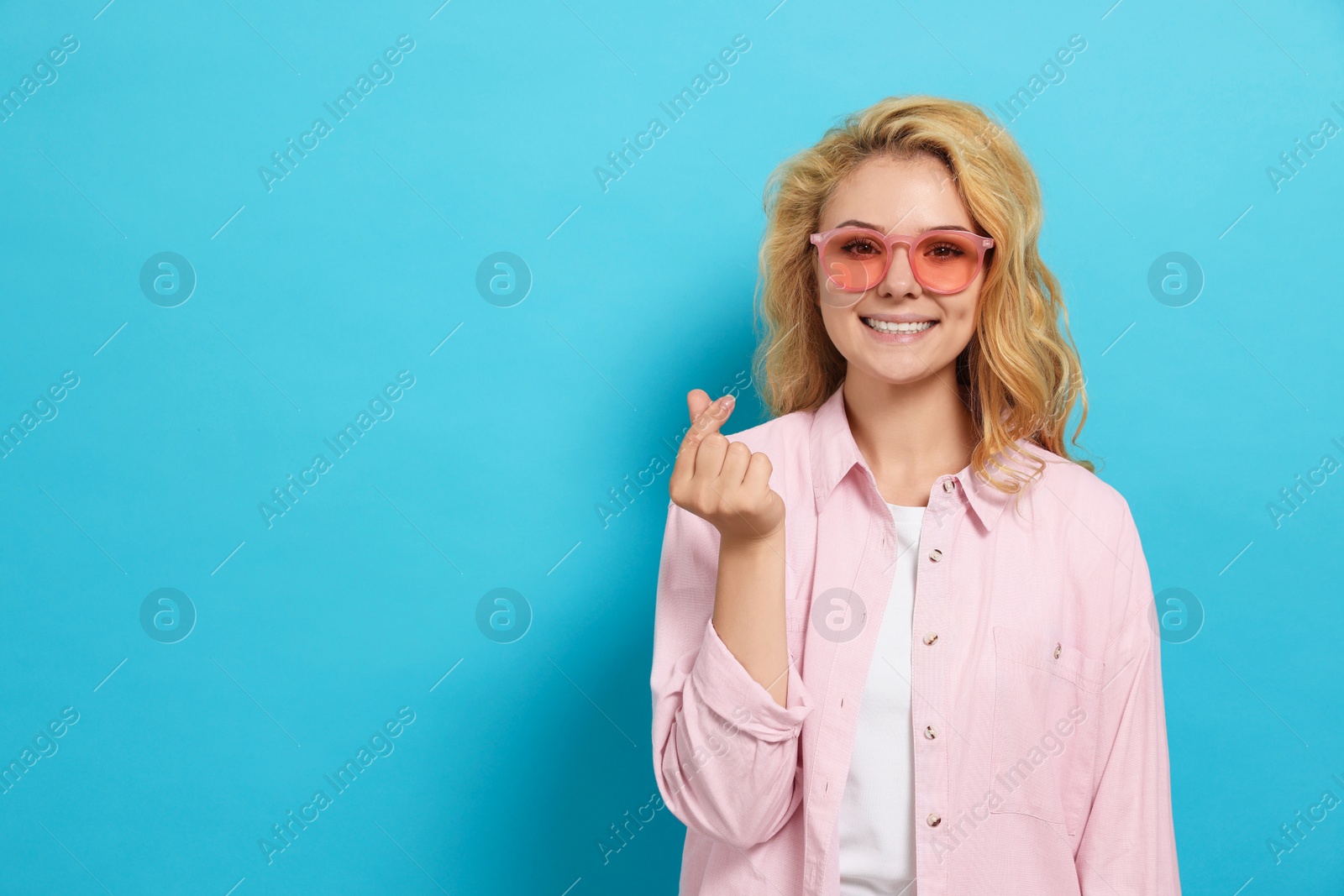 Photo of Happy young woman showing heart gesture on light blue background. Space for text