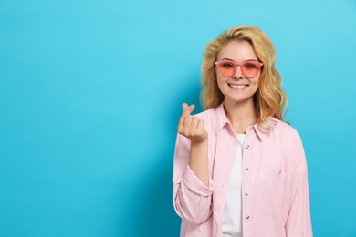 Happy young woman showing heart gesture on light blue background. Space for text
