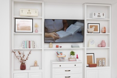 Photo of TV and shelves with different decor in room. Interior design