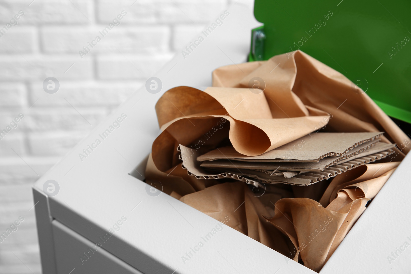 Photo of Trash bin with paper and cardboard near brick wall, closeup. Recycling concept