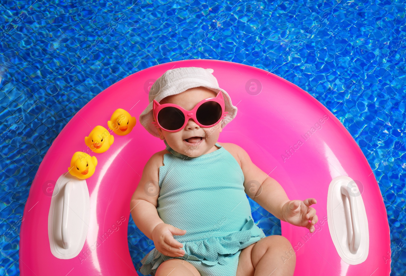 Image of Cute little baby with inflatable ring in swimming pool, top view