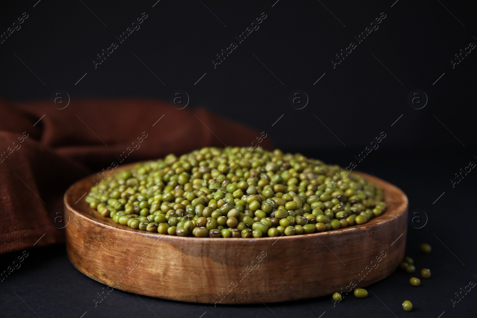 Photo of Wooden bowl with green mung beans and napkin on black background, closeup