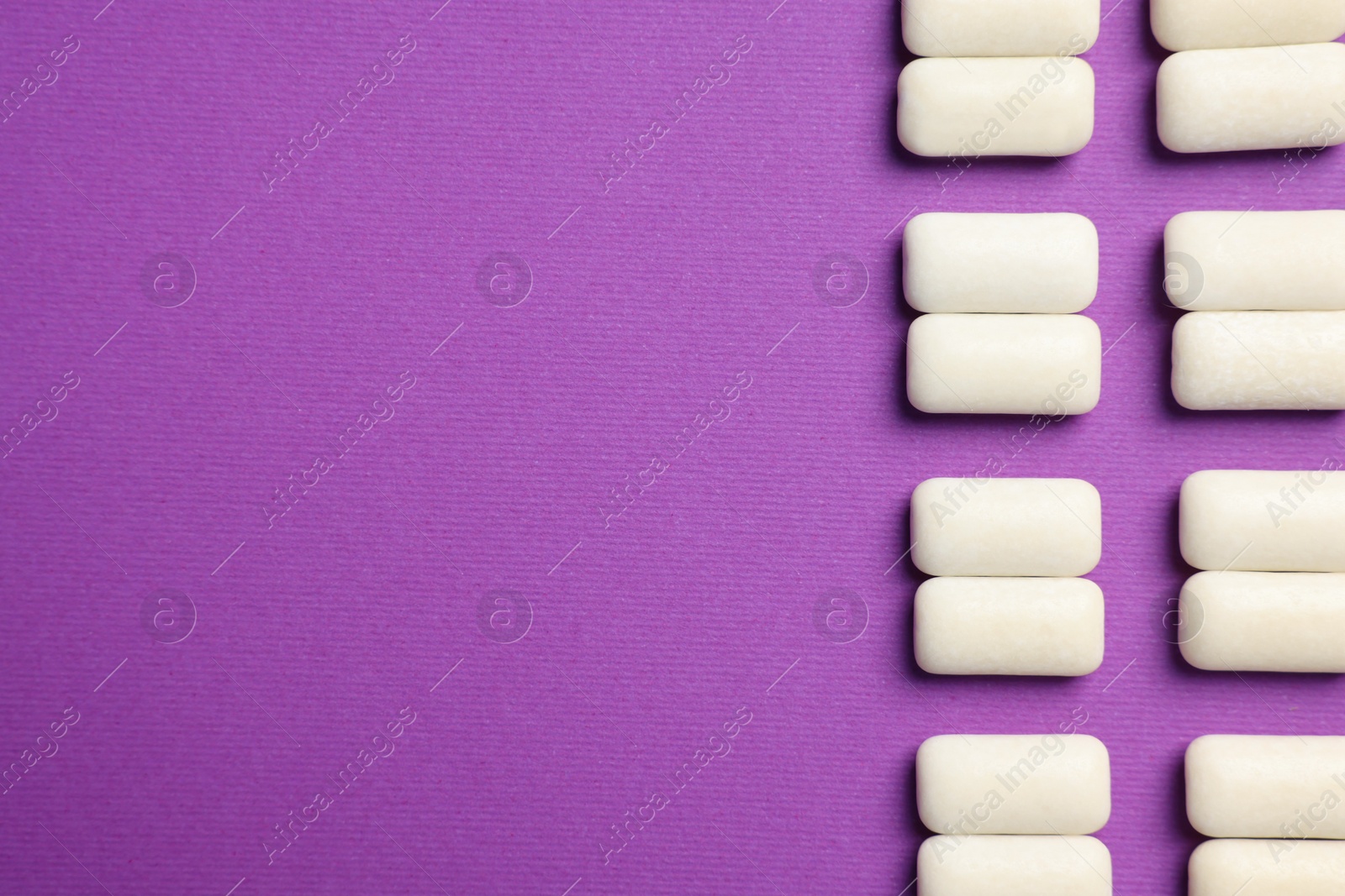 Photo of Tasty white bubble gums on purple background, flat lay. Space for text