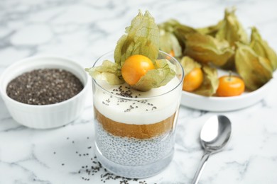 Photo of Delicious chia pudding decorated with physalis fruit on white marble table