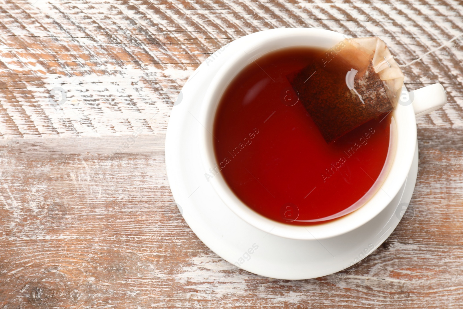Photo of Tea bag in cup with hot drink on wooden rustic table, top view. Space for text