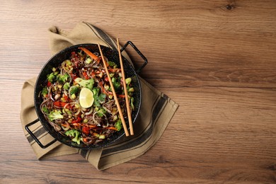 Photo of Stir-fry. Tasty noodles with meat in wok and chopsticks on wooden table, top view. Space for text