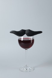 Photo of Glass of red wine with funny fake mustache on grey background