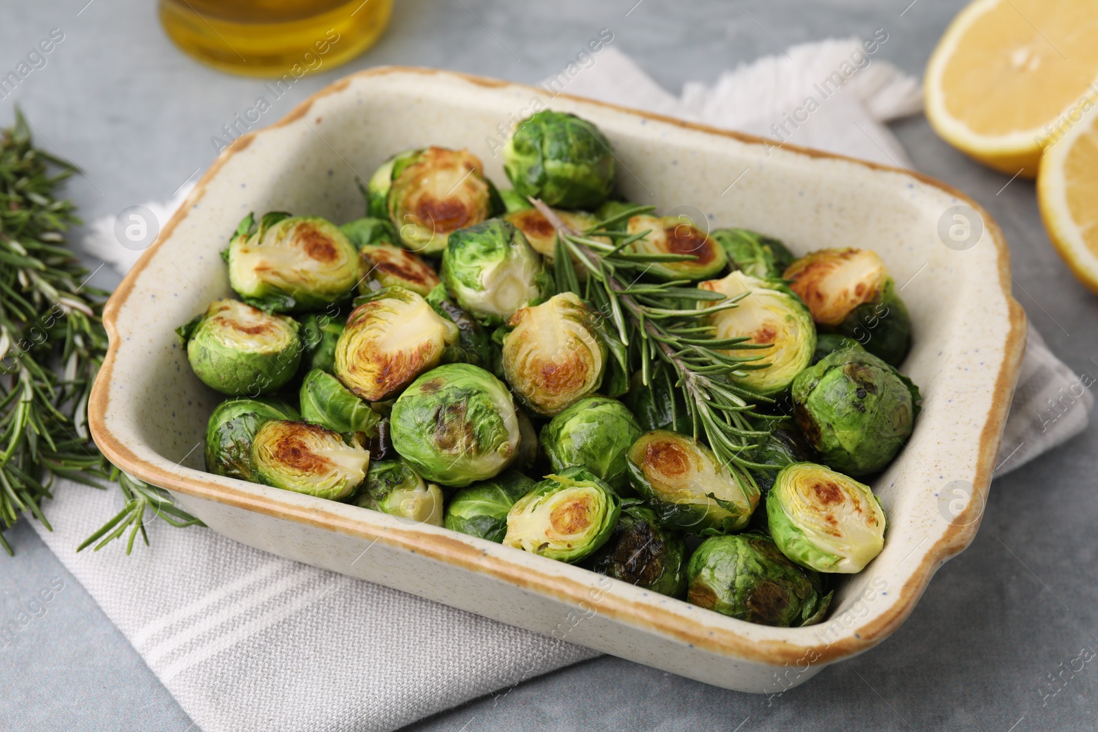 Photo of Delicious roasted Brussels sprouts and rosemary in baking dish on grey table